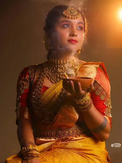 A creative and atmospheric shot of a client in a yellow and red bridal saree, holding a traditional incense bowl.