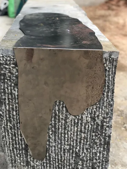 The "Kagami" bench during its creation, showing the process of fitting the polished steel inlay into the hand-dressed stone. This highlights the craftsmanship behind the sculptural piece.