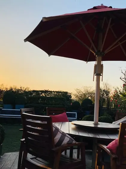 Transform your terrace into a green paradise. This sunset view shows a cozy seating area under a bright red umbrella, surrounded by lush hedges and topiary, creating a perfect escape right at home.