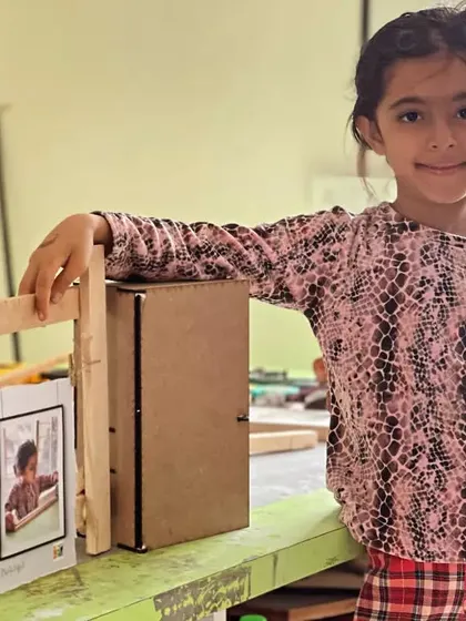 A proud student poses with her completed wooden photo frame, a project that teaches basic construction skills.