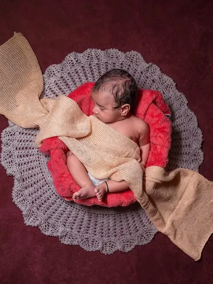 This creative setup styles the baby to look like a piece of candy, using a red prop and beige fabric for the "wrapper". It's a fun and whimsical way to capture how sweet your newborn is.