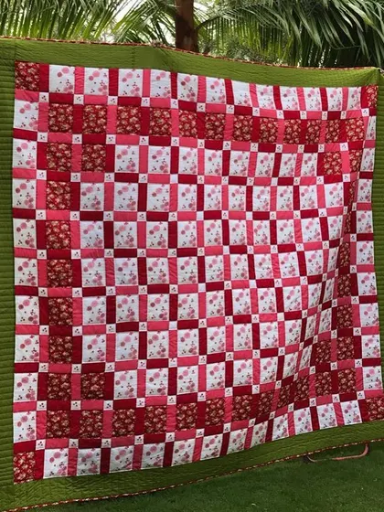 A classic "Irish Chain" quilt in red and white floral fabrics, displayed in a garden setting.