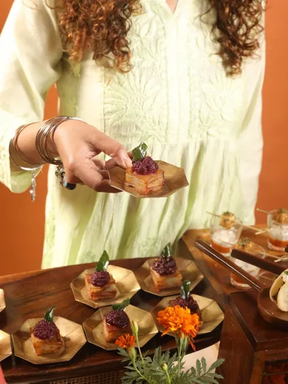 A guest holding a bite-sized appetizer of layered potato and beetroot on a leaf-shaped plate. This highlights our use of eco-friendly and aesthetically pleasing serveware.