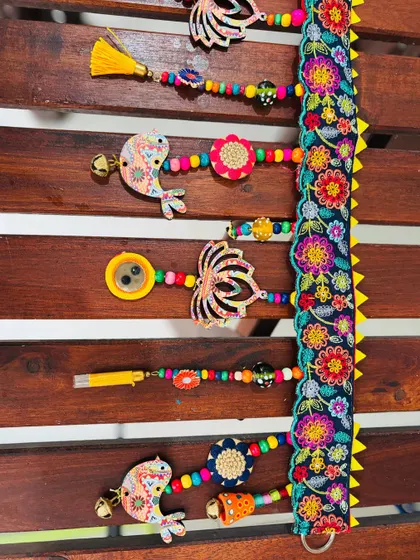 A close-up of the 'TAMAARA' toran. Notice the details on the embroidered lace, the wooden beads, and the original lotus and bird artwork printed on the cutouts.