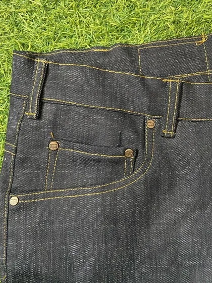 Detail of the front pocket on a pair of custom raw denim jeans, showing the clean, strong stitching and classic rivet hardware.
