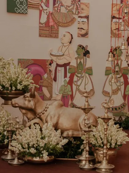 A decor corner featuring a brass Nandi statue, traditional lamps (diyas), and arrangements of white tuberoses, all set against a backdrop of Indian folk art. This is a perfect blend of tradition and aesthetics.