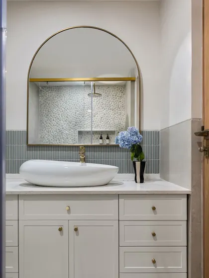 The primary bathroom features a beautiful arched mirror and a mix of pebble and subway tiles in soft blue-grey tones. The design creates a spa-like atmosphere that is both refreshing and serene.