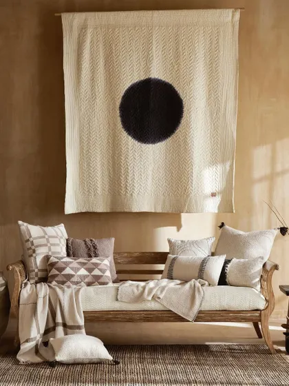 A duplicate of image 22, this shot captures a living room setting with a focus on texture and minimalist art. The natural light brings out the details in the wooden daybed, patterned cushions, and woven rug.