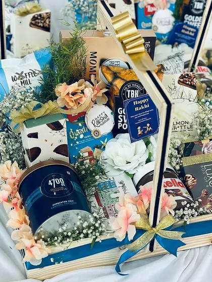 Our luxury snack hampers are designed to delight the senses. This overflowing pinewood basket is artfully arranged with a premium selection of gourmet popcorn, Nutella, cookies, and fine chocolates, adorned with fresh flowers for a truly impressive presentation.