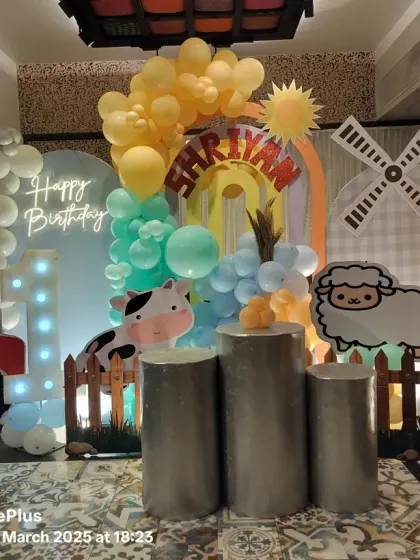 We brought the countryside to the city with this farm-themed first birthday. The setup includes a tractor cutout, a windmill prop, cute farm animal characters, and a "1" marquee number against a backdrop of soft-colored balloons.