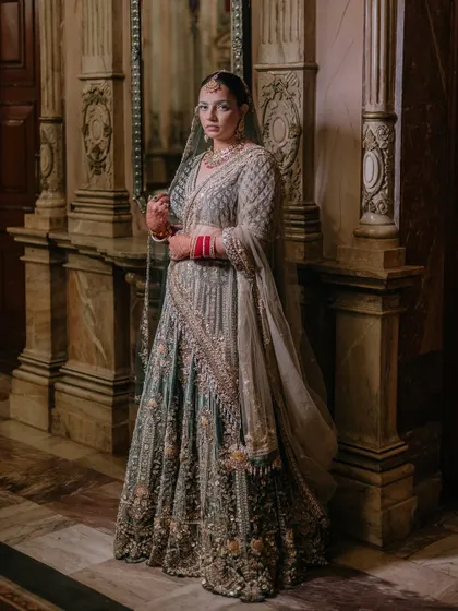 A full-length portrait of the bride in her heavily embroidered lehenga, standing in a grand, marble-pillared hall in Kathmandu.
