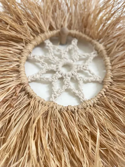 This bohemian wall decor is made from natural raffia grass and features a macrame mandala pattern in the center. It's a beautiful, rustic piece that adds texture and warmth to a wall.