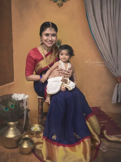 A formal portrait of a mother and her son in their Krishna-themed attire. The rich colors of the saree and the detailed setup create a regal and timeless image.