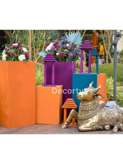 A decorative corner at a Vrindavan-themed party, featuring a brass Nandi statue, colorful pedestals, and floral arrangements.