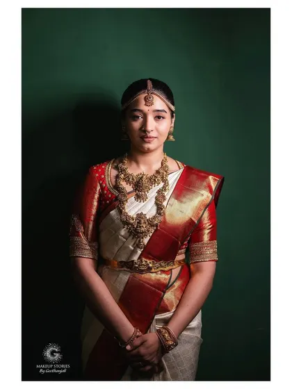 A full portrait of Priyanka against a simple green backdrop. This shot highlights the classic elegance of her white and red wedding saree and the understated beauty of her natural makeup look.