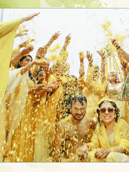 A fantastic group shot from a Haldi ceremony, with everyone joyfully tossing flower petals into the air. This is a perfect picture of collective happiness.