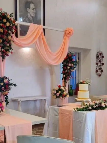 A charming cake table setup for an intimate celebration. The table is decorated with peach-colored runners and drapes, and surrounded by beautiful floral arrangements.