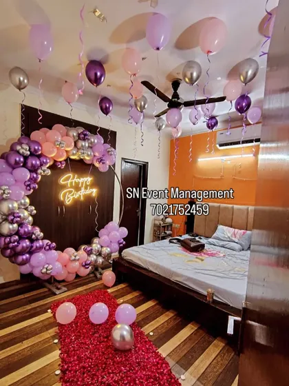 An elaborate and romantic birthday room decoration. This setup includes a full balloon ring in purple and pink, balloons on the ceiling, and a path of rose petals leading to the bed.