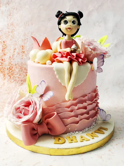 We design a cake fit for a modern princess. A custom-made fondant girl with glasses and a pink dress sits among fresh roses, delicate butterflies, and a pink crown, creating a personalized and enchanting birthday centerpiece.