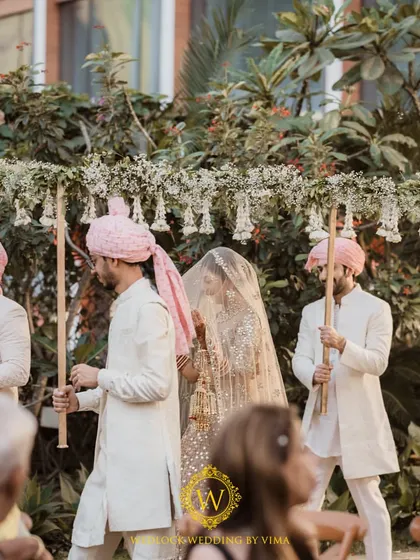 The bride's grand entrance under a beautiful phoolon ki chadar made of fresh white flowers and greenery. This moment was part of a minimalist wedding with an elegant white and green theme.