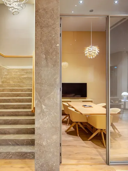 This workspace is a formal meeting room within a larger home, enclosed by glass walls to provide acoustic privacy without sacrificing visual connection. The sculptural pendant light adds a touch of modern elegance.