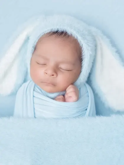A close-up of a sleeping baby in a fluffy blue bunny hat. The simplicity of the shot highlights the baby's peaceful features.