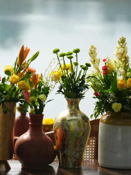 A collection of colorful flowers in various rustic and modern vases, used as a centerpiece for a Haldi lunch.