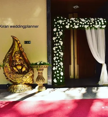 An elegant entrance for an engagement party, featuring a floral arch, sheer white drapes, and a traditional golden Ganesha idol to welcome guests.