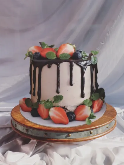 A Nutella hazelnut cake with a chocolate drip, decorated with fresh strawberries, blueberries, and mint leaves.