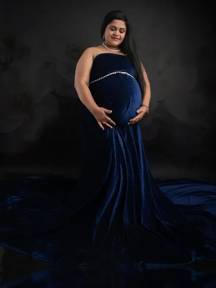 A classic maternity portrait in a luxurious royal blue velvet gown. The fabric drapes beautifully, and the soft lighting creates a serene and elegant mood.