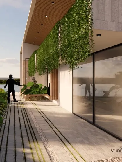 This corridor along the waterfront home is an exercise in transparency and reflection. The large glass panels reflect the sky and water, while a curtain of hanging plants adds a layer of green, blurring the edge of the building.
