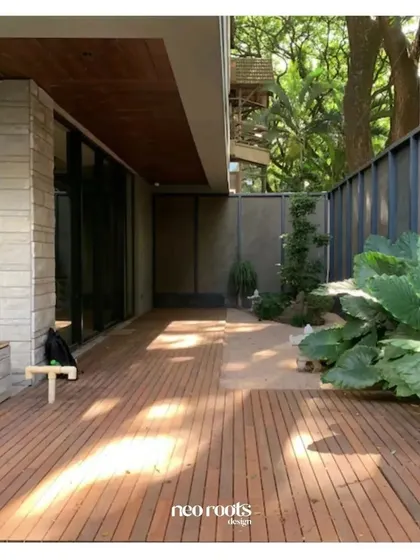 An expansive wooden deck provides a warm and inviting outdoor living space adjacent to this modern home. The clean lines of the deck are complemented by large-leafed plants, creating a contemporary yet natural feel.