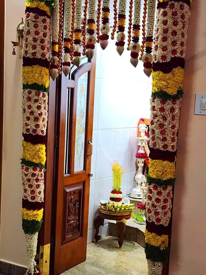 A full view of a main door decorated with colorful flower columns and hanging tassels for a housewarming pooja.