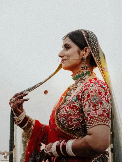 A side-profile portrait that highlights the bride's jewelry and the details of her dupatta. Her gentle smile and the clean background make for a timeless image.
