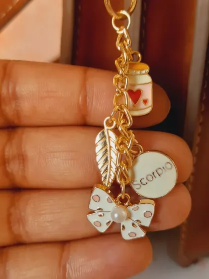 A close-up of a custom bag charm I made, featuring a Scorpio zodiac charm, a bow, a feather, and a cute little jar of hearts.