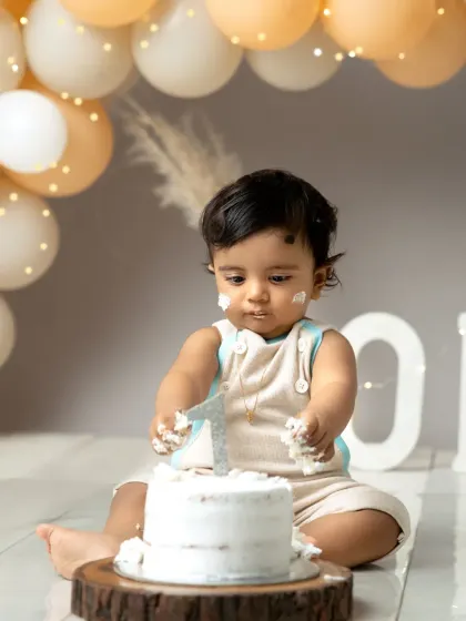 A moment of intense focus on the cake. Dressed in adorable overalls, this little one is ready to dive into his first birthday celebration.