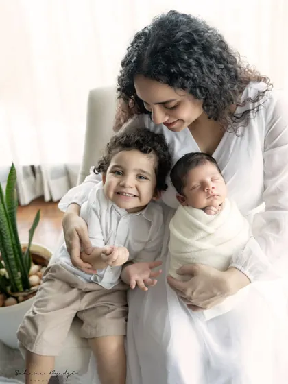 Welcoming a new baby is a joy for the whole family. Here, a proud big brother smiles for the camera while his mother cradles their precious newborn, a perfect sibling and newborn portrait.