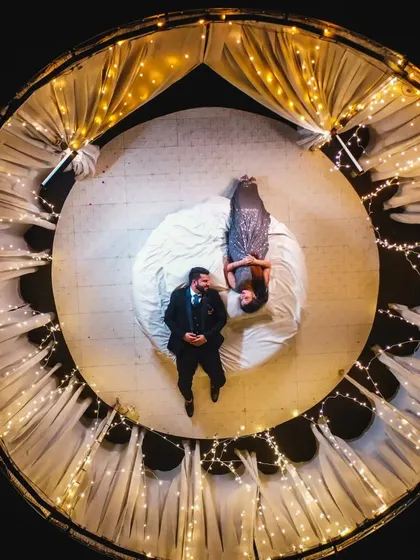 A creative top-down shot of a couple lying on a circular stage decorated with fairy lights, creating a magical and unique portrait.