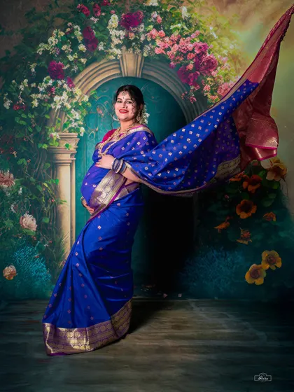 The timeless elegance of a traditional saree maternity shoot. This studio portrait uses dramatic posing and lighting to highlight the beauty of the mother-to-be and her gorgeous blue silk saree.