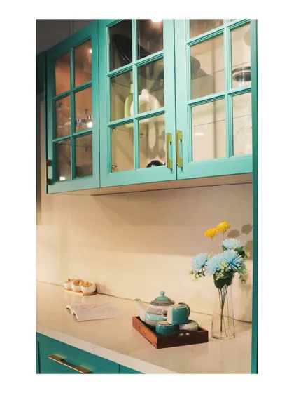 A close-up of a European-style crockery unit with a Duco finish in a vibrant teal, featuring glass-fronted doors.