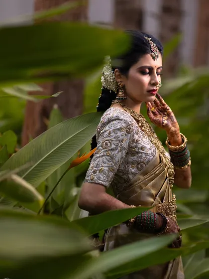 An elegant portrait of a South Indian bride in a golden saree, surrounded by lush greenery, capturing her grace and beauty.