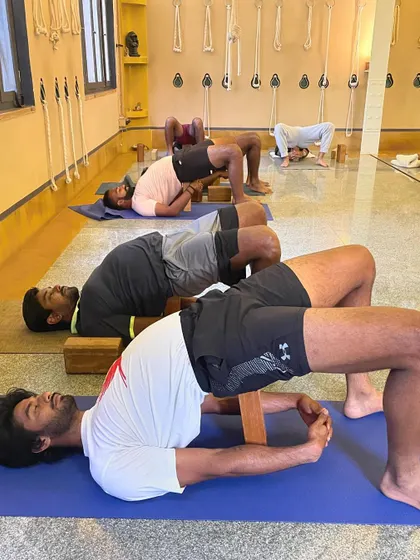Close-up on the alignment of supported Bridge Pose. The block placement and hand clasp are specific details that ensure the chest opens correctly and the neck remains safe.