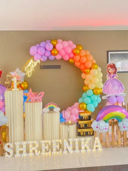 A rainbow and princess-themed birthday party. The setup features a rainbow balloon arch, princess cutouts, and cloud and rainbow props.