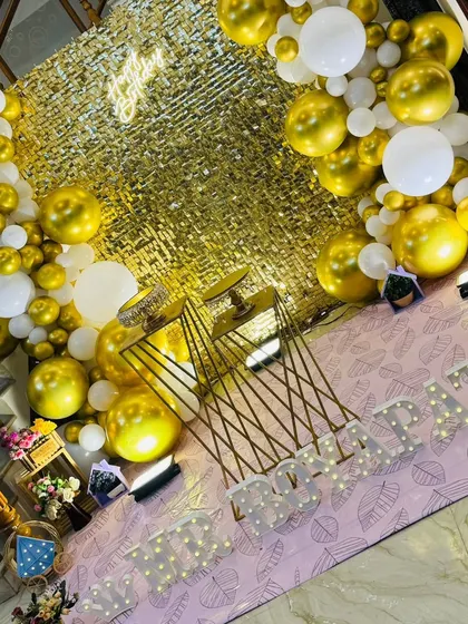 An angled shot highlighting the depth of the balloon arch against the gold sequin wall. The warm uplighting makes the gold tones pop, creating a luxurious feel.