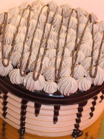 A beautifully decorated eggless Nutella cake. The top is covered in intricate piping work with a drizzle of Nutella for extra flavor.