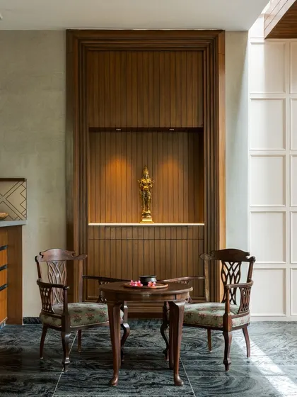 A small, intimate seating area featuring a traditional puja niche carved from wood. This space blends modern design with cultural elements, using dark marble flooring and warm lighting.