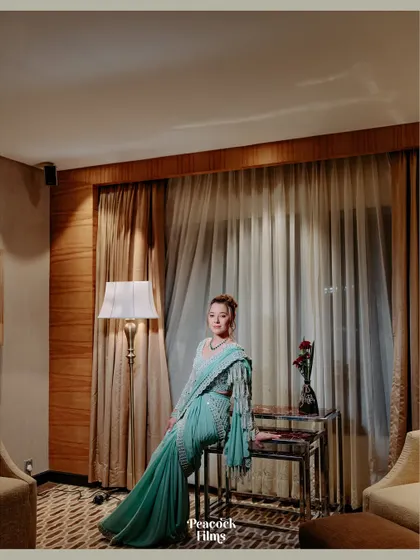 A full-length portrait of the bride, showcasing her stunning sea-green saree and the elegant decor of the room. A picture of pure grace.
