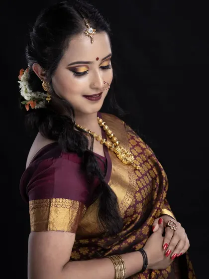 A side view of a beautiful braided hairstyle. The hair is swept to one side and styled into a thick braid, adorned with flowers, which looks elegant with the traditional saree.