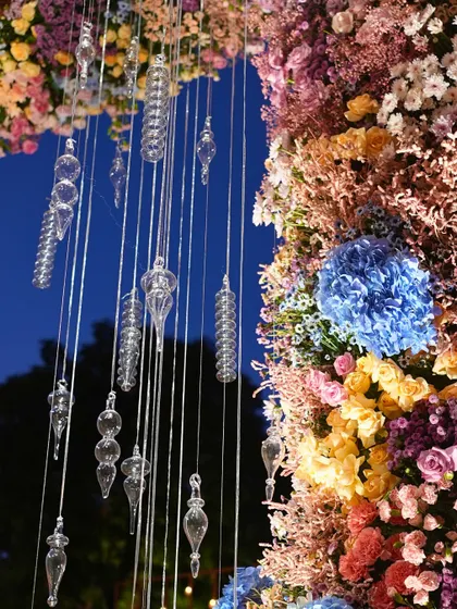 A detailed shot of the floral arrangement on the mandap pillars, showing the rich textures and colors of the flowers mixed with delicate hanging glass ornaments.