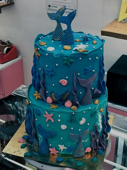 An underwater adventure in cake form. This two-tiered mermaid cake is decorated with fondant mermaid tails, starfish, and seashells in shades of blue and purple.